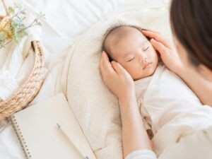赤ちゃんの名付けを考える時間をイメージした、明るい光の中で眠る赤ちゃんと優しく見守る親の手元を写した写真風画像
