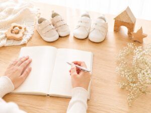 兄弟・姉妹の名前の画数や統一感を考える場面を、2足のベビーシューズと名付けノート、ペンで表した明るい写真風画像